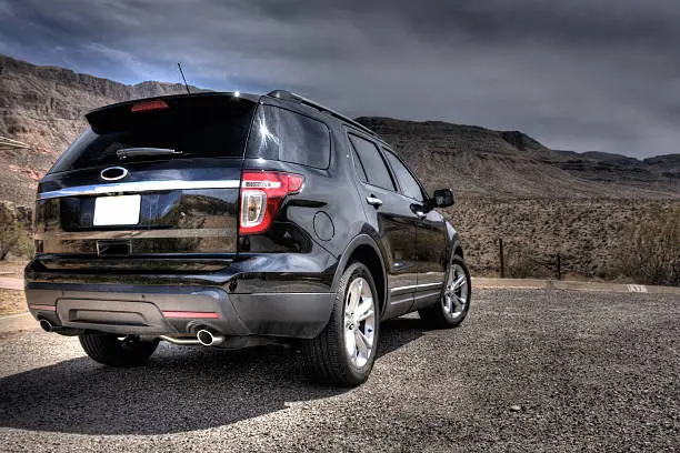 A large, all-American SUV is parked on hot asphalt against a background of desert scrub and mountains under a hot blue sky. Given the HDR treatment to bring out the liquid black gloss of the paintwork.