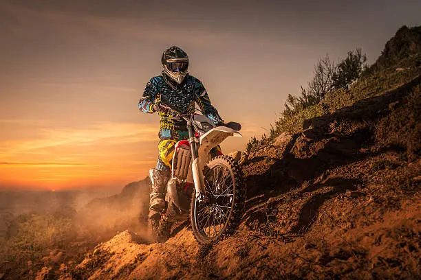 Enduro rider climbing a high slope against a beautiful sunset on a seascape.