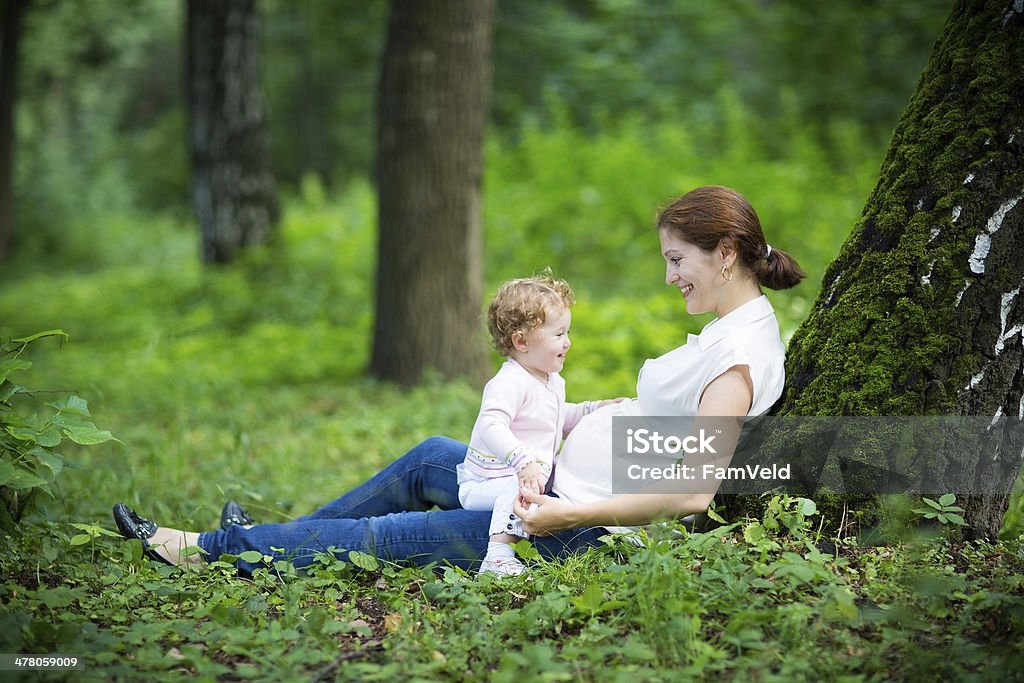 Young pregnant mother playing with her toddler daughter Grass Stock Photo