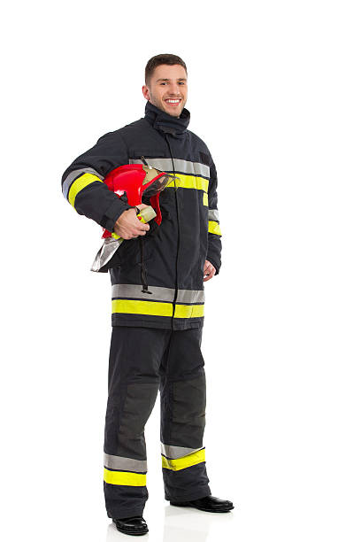 feuerwehrmann posieren mit helm unter dem arm - isolated on white full length red protection stock-fotos und bilder