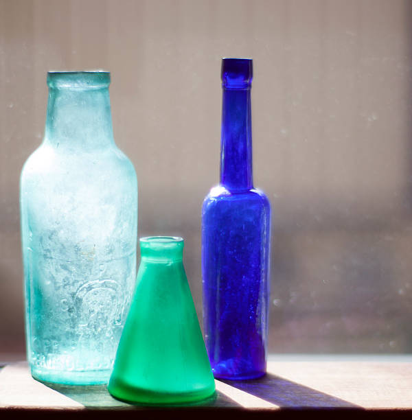 Ashtray with cigarette butts on a windowsill next to a empty bottle