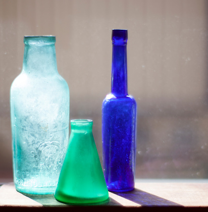Four (4) different colored bottles on windowsill casting colored shadows from the sun.