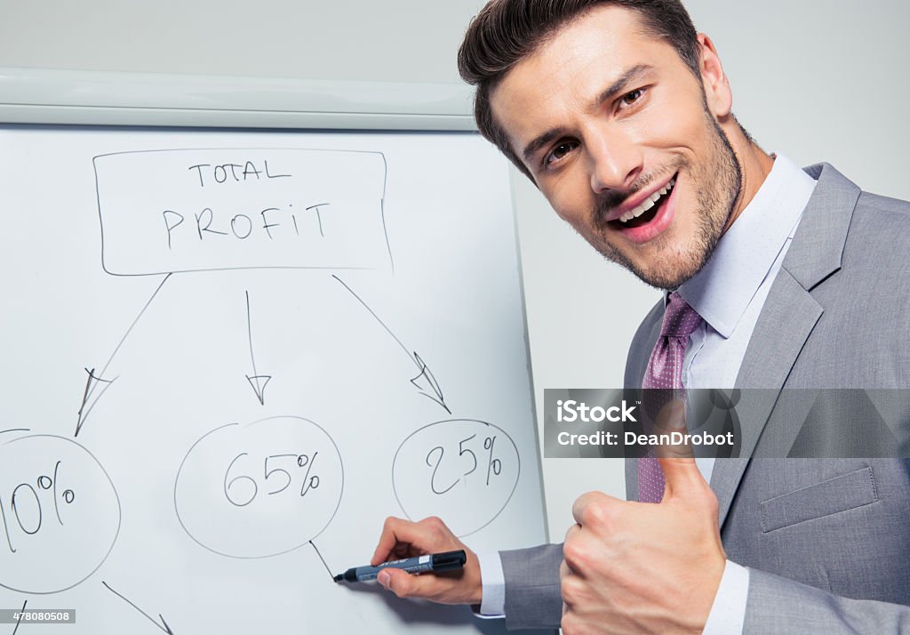 Happy businessman writing on a flipchart Happy businessman writing on a flipchart and showing thumb up. Looking at camera 2015 Stock Photo