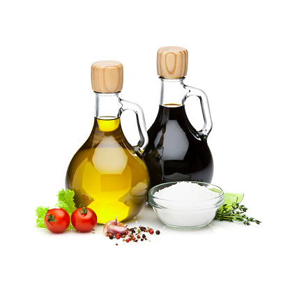 Oil and vinegar, the background is white. the oil and vinegar are placed in a vintage glass cruet. there is some oil in a glass bowl
