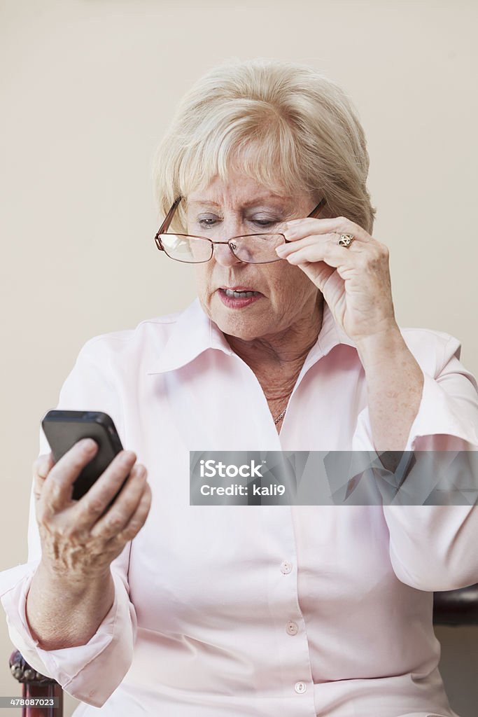 Senior mujer mirando a un teléfono móvil - Foto de stock de Descontento libre de derechos