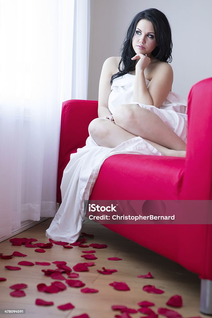 Schöne Frau sitzt auf dem roten Sofa mit Rosenblättern - Lizenzfrei 20-24 Jahre Stock-Foto