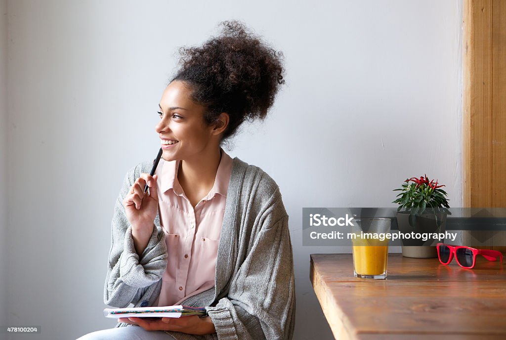 Happy young woman sitting at home with pen and paper Portrait of a happy young woman sitting at home with pen and paper Contemplation Stock Photo