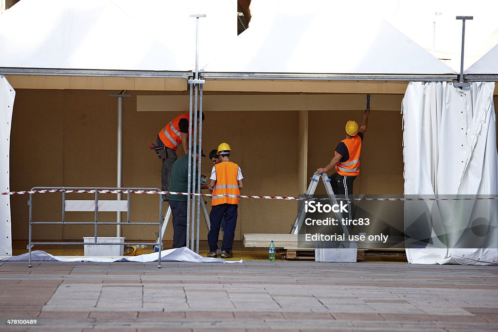 Workmen constructing a marquee Bologna, Italy - November 8, 2012: Workmen in reflective clothing discussing the plans for constructing a marquee in one of the public squares in the italian city of Bologna. Two of the men are standing on stepladders. Adult Stock Photo