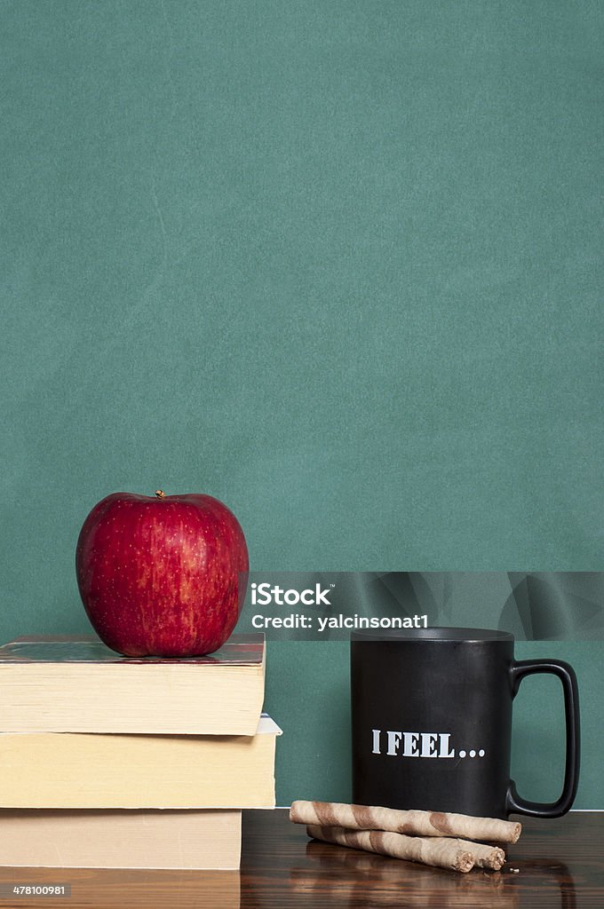 Education books coffee mug wafer rolls and apple in front of green chalkboard Back to School Stock Photo