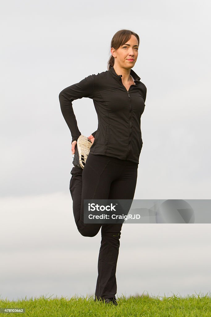 Female Athlete Stretching A female athlete stretching. She is wearing her training clothes on a cold winter morning. Grey sky back ground. 20-29 Years Stock Photo