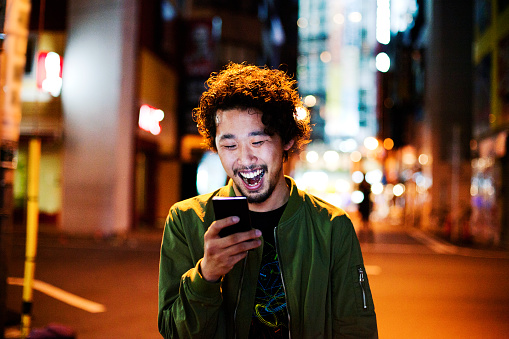 Happy japanese young man with smart phone at night, Tokyo.