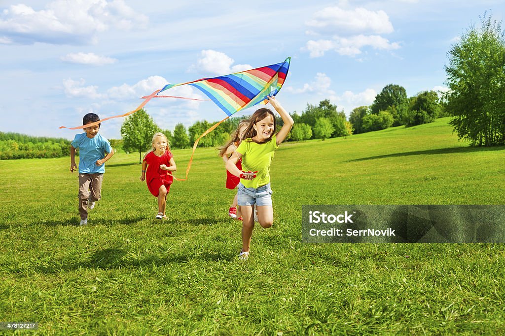 Group of kids with kite Four little kids running in the park with kite happy and smiling Child Stock Photo
