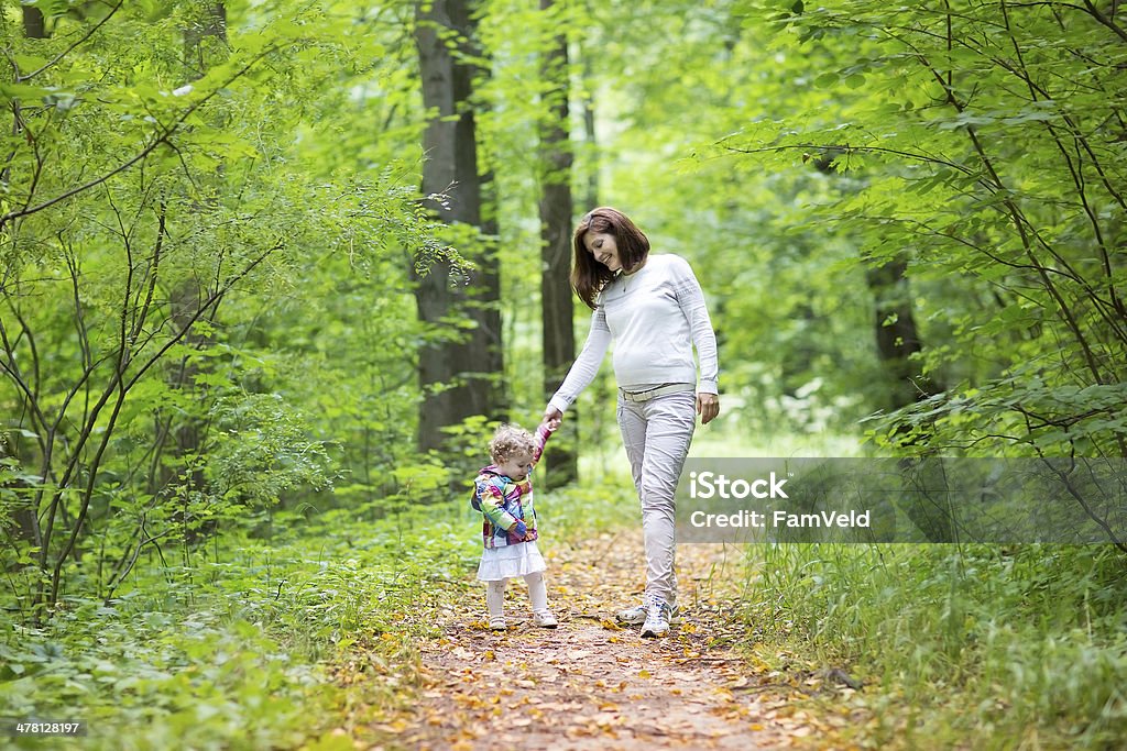 Beautiful pregnant woman and her baby daughter walking in park Beautiful young pregnant woman and her baby daughter walking in an autumn park 12-17 Months Stock Photo