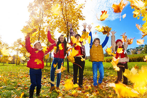 Group of five kids, boys and girls throwing autumn maple leaves in the park on sunny day