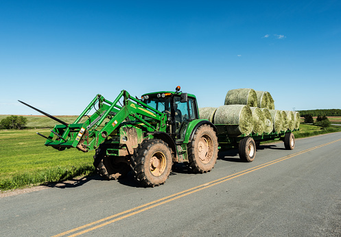 Milford, Canada - June 15, 2015: A farmer driving a John Deere tractor hauls a load of freshly baled hay back to farm.