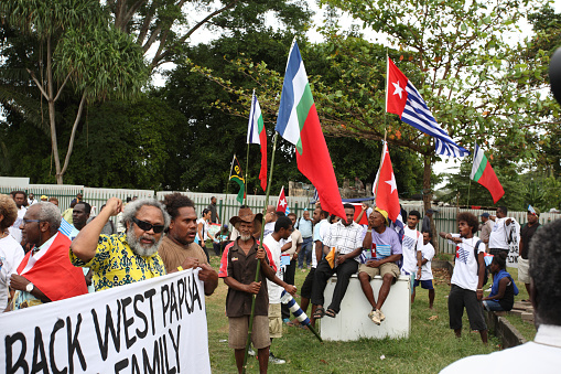 Honiara, Solomon Islands, June 19, 2015.a group of men and demonstrators sit and stand with banners and flags at a solidarity meeting demanding full membership for West Papua in the Melanesian Spearhead Group