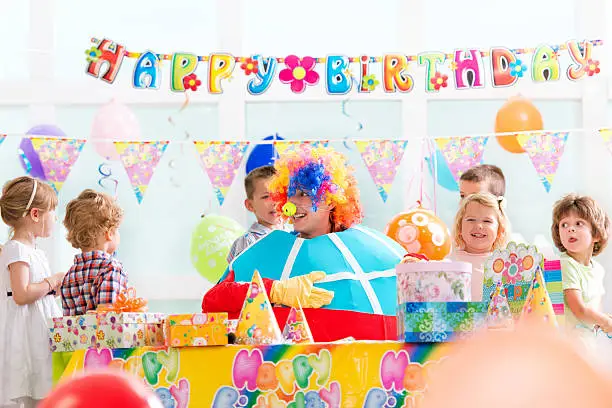 Large group of happy children playing with clown at birthday party.