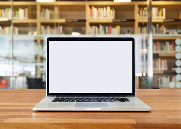 Laptop on table, on bookshelf background,blank screen,library interior