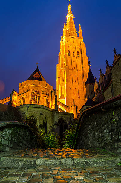 The Onze Lieve Vrouwekerk in Brugge seen at night looking across a bridge on the canalThe Onze Lieve Vrouwekerk in Brugge seen at dusk looking across a bridge on the canal
