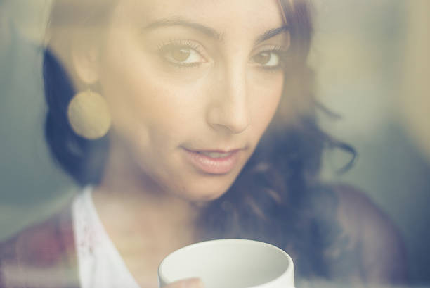 istock beautiful woman with cup facing through window 478151257