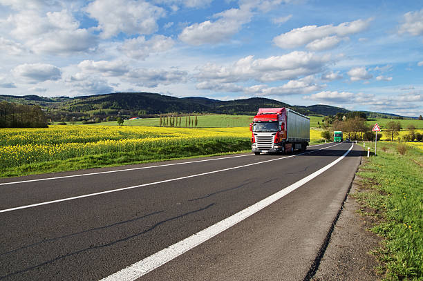 istock Red and green trucks on the road between rapeseed field 478151690