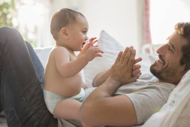 Father playing with baby boy on bed stock photo
