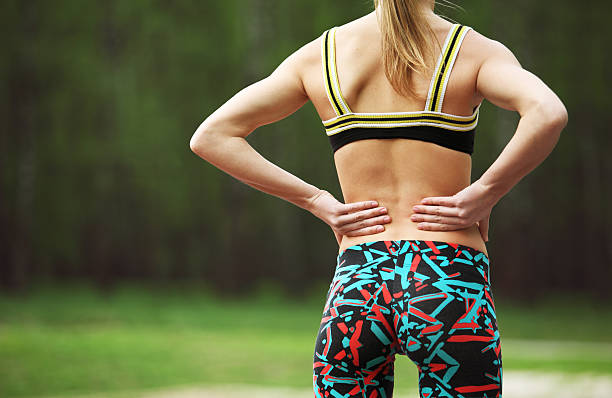Athletic young woman rubbing muscles of lower back after jogging stock photo