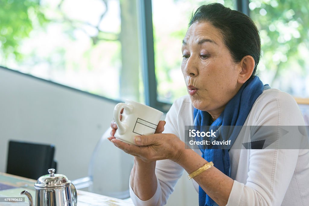 Happy Senior Japanese Woman Drinking Hot Coffee in a Cafe Happy senior Japanese woman sitting drinking coffee in a cafe in Tokyo 2015 Stock Photo