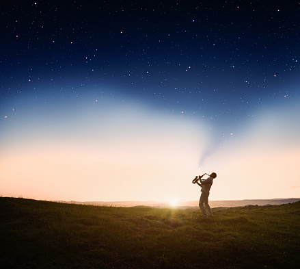 Man playing a saxophone at sunset with stars emerging from the saxophone