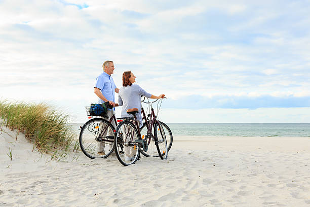 熟年カップルビーチでのアウトドアアクティビティー - retirement mature couple couple bicycle ストックフォトと画像