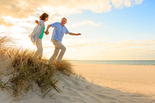 sunset – szczęśliwy dojrzała para na plaży - senior couple senior adult walking action zdjęcia i obrazy z banku zdjęć