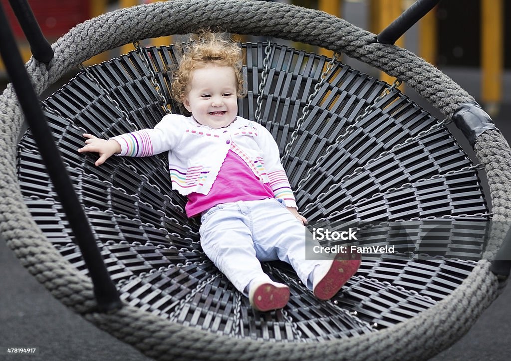 Cute laughing baby girl at net swing on the playground Cute laughing baby girl on a net swing enjoying a sunny day on the playground Activity Stock Photo