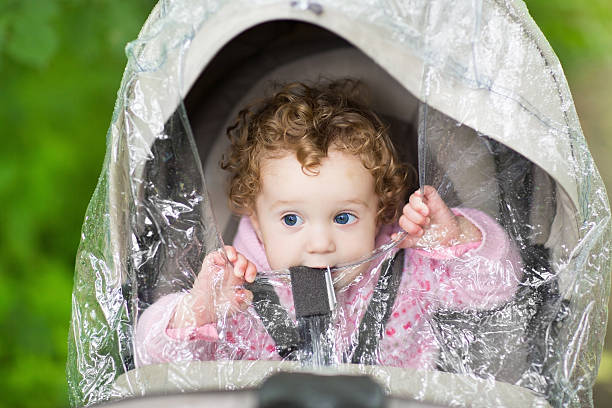 istock Cute baby girl sitting in stroller under plastic rain cover 478210569