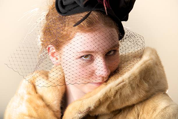 Redhead smiling shyly in black veiled hat and fur coat