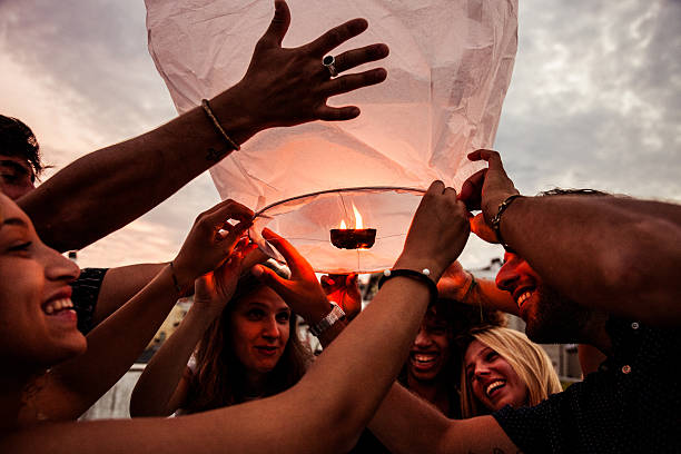 Friends having a lot of fun at birthday party outdoor starting a chinese lantern at the end of the event.