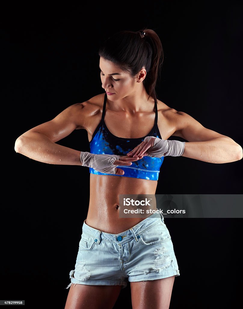 athletic woman with muscular build sweat and muscular woman in sports bra and shorts,wearing fighting tape on her hands. 20-24 Years Stock Photo