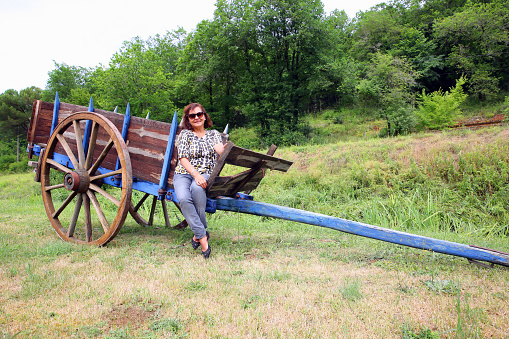 Mature smiling hispanic woman sitting on antique haycart in the Dordogne in France