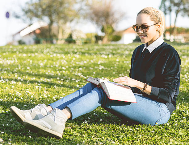 istock Blond student girl reading book on grass 478222678