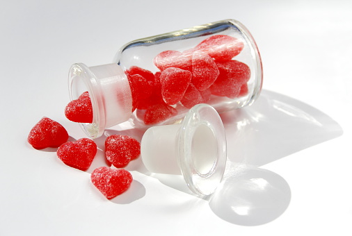 Old glass bottle with red heart shape gummy spilling on white background