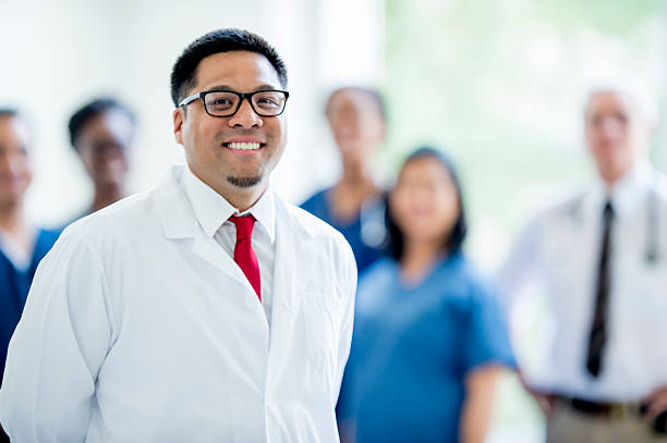 Doctor and his Team A doctor standing in front of a multi-ethnic group of medical professionals; inside of an office building; smiling and looking at the camera. red medical scrubs stock pictures, royalty-free photos & images