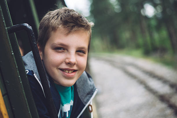 Young and handsome boy enjoys riding an old train. He looks through the open window and smiles. Photo was edited to aquire old film look .