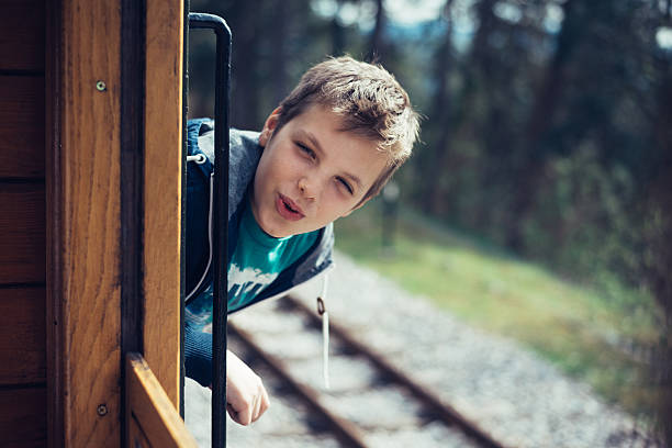 Young and handsome boy enjoys riding an old train. He looks through the open window and smiles. Photo was edited to aquire old film look .