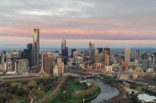 The Yarra River passes through the centre of Melbourne, dividing the central business district on the right (north) side from the Southbank area on the left. The bridge is Princes Bridge. On the left from the bottom of frame is the King’s Domain, behind which from the left are the rectangular National Gallery of Victoria, the Arts Centre with its distinctive spire and the round flat-topped Hamer Hall concert hall. Behind looms the gold-tipped Eureka Tower, Melbourne’s tallest building. North of the river lies Flinders Street Station and Federation Square