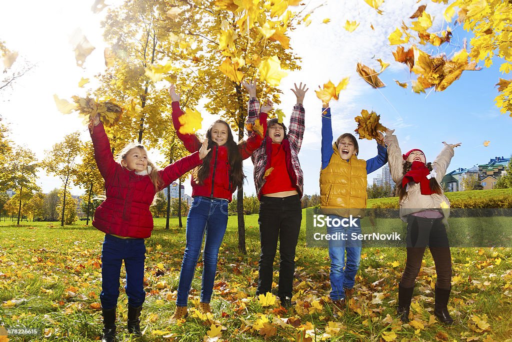 Kids enjoying autumn maple park Group of five kids, boys and girls throwing autumn maple leaves in the park Autumn Stock Photo