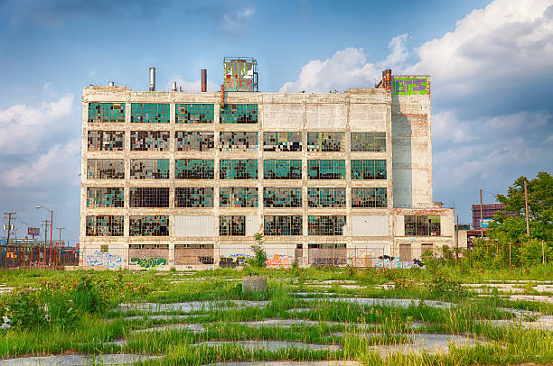 Detroit Factory Ruins Detroit, USA - June 9, 2015: The old Fisher Body Works factory  in the Highland Park of Detoit area shows the post-industrial plight of the city after the factory was closed in the 1980s. The buildings windows are broken, the walls are covered with graffiti, and the parking lot is overgrown with weeds. highland park michigan stock pictures, royalty-free photos & images