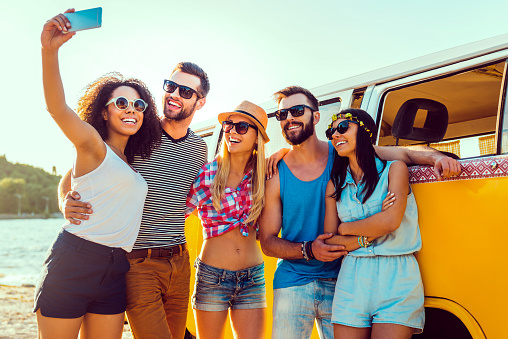 Group of happy young people bonding to each other and making selfie while standing near their retro mini van