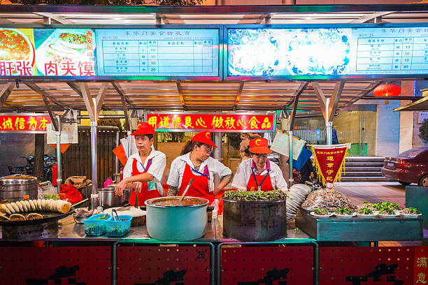 Beijing nightlife cooks at Donghuamen street market food stall China Beijing, China - 27th September 2013: Cooks at a colourful street food stall in a night market in the centre of Beijing, China's vibrant capital city. wangfujing stock pictures, royalty-free photos & images