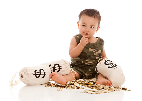 Adorable mixed race baby boy playing with plastic gold coins and money bags.  One gold coin in his mouth.  Isolated on white.
