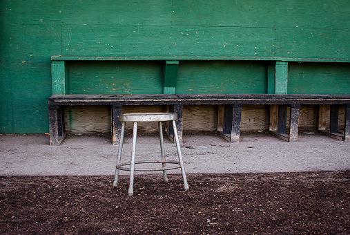 An empty stool sits in front of an old, empty dugout at a high school baseball field. Adobe RGB color space.