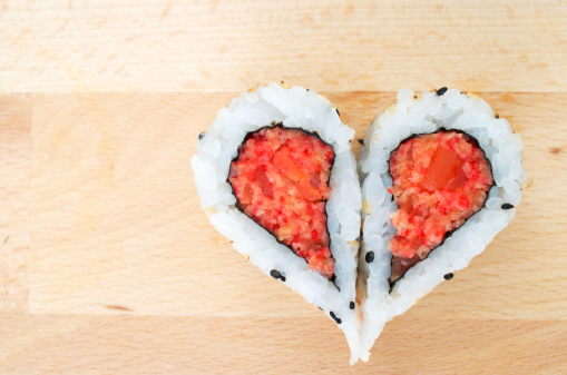 Two pieces of sushi forming the heart shape on wooden cutting board